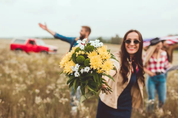 Jeune femme heureuse montrant bouquet de fleurs à la caméra avec des amis heureux marchant derrière — Photo de stock