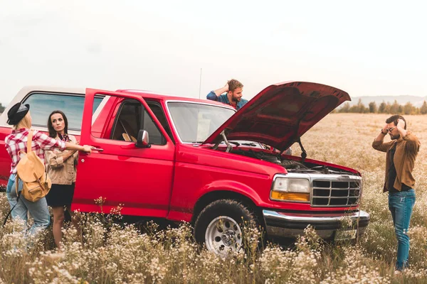 Grupo de jóvenes viajeros de coches que tienen problemas con el motor y atrapado en el campo - foto de stock