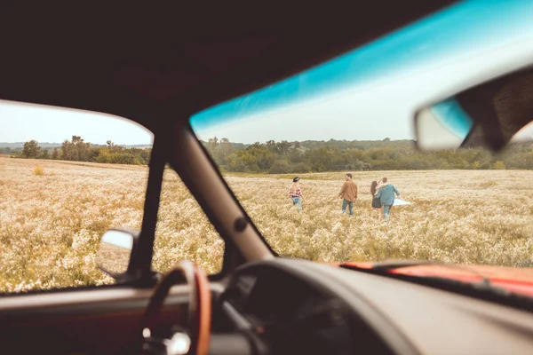 Вид из автомобиля на группу молодых людей, идущих по цветочному полю во время автомобильной поездки — стоковое фото