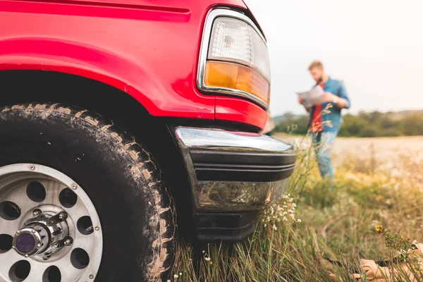 Primo piano di camion rosso in piedi sul campo con l'uomo sfocato che naviga con la mappa sullo sfondo — Foto stock