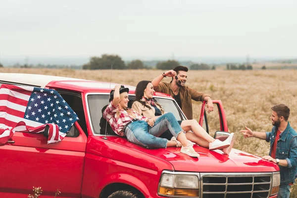 Grupo de jóvenes viajeros americanos en coche relajándose en el campo de flores - foto de stock