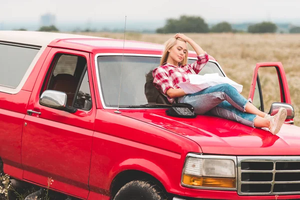 Bela jovem mulher relaxante no capô do carro no campo — Fotografia de Stock