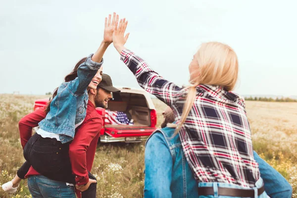 Rear view of young women piggybacking on boyfriends and giving high five in flower field — Stock Photo