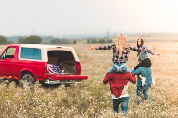 Junge Frauen bei Autofahrt auf Schultern von Freunden im Feld — Stockfoto