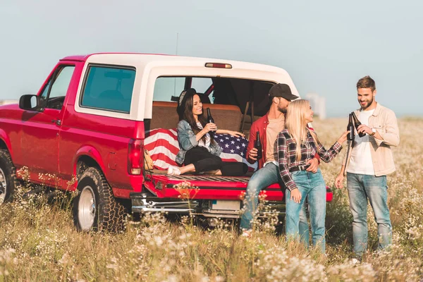 Gruppe junger Leute klappert Bierflaschen, während sie im Kofferraum eines Autos auf einem Blumenfeld sitzen — Stockfoto