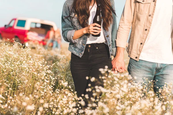 Cropped shot of couple holding hands and walking by flower field — Stock Photo