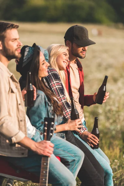 Group of young people drinking beer while sitting in car trunk in field — Stock Photo