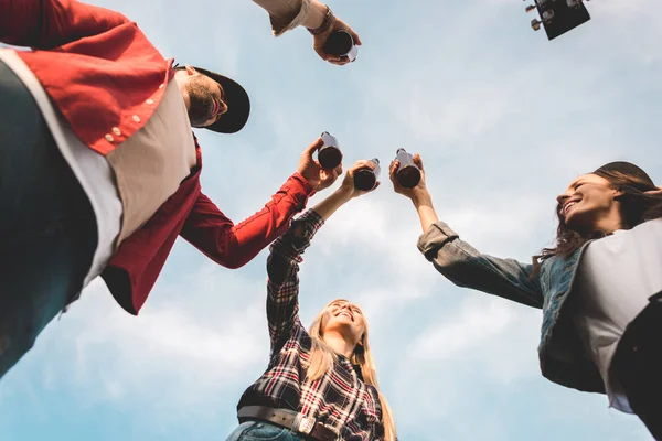 Вид снизу группы молодых людей, звенящих бутылками пива перед облачным небом — стоковое фото