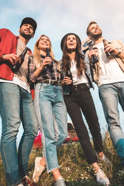 Vista dal basso di gruppo di giovani con bottiglie di birra e chitarra sul campo — Foto stock