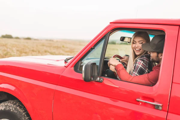 Happy young couple sitting on drivers seat together and driving truck by field — Stock Photo