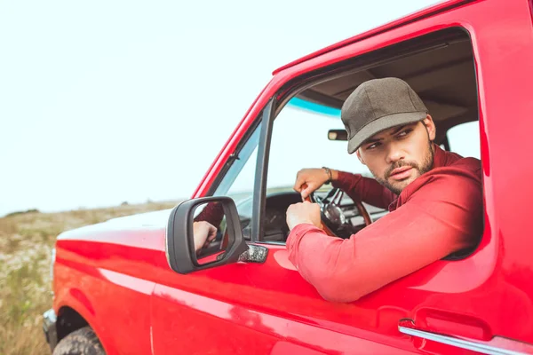 Beau jeune homme conduisant vieux camion rouge dans le champ et regardant en arrière — Photo de stock