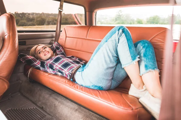 Bela jovem deitada no banco de trás do carro vintage no campo — Fotografia de Stock