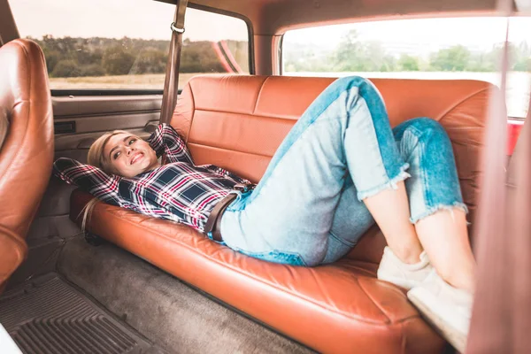 Bella giovane donna sdraiata sul sedile posteriore di auto d'epoca in campo — Foto stock