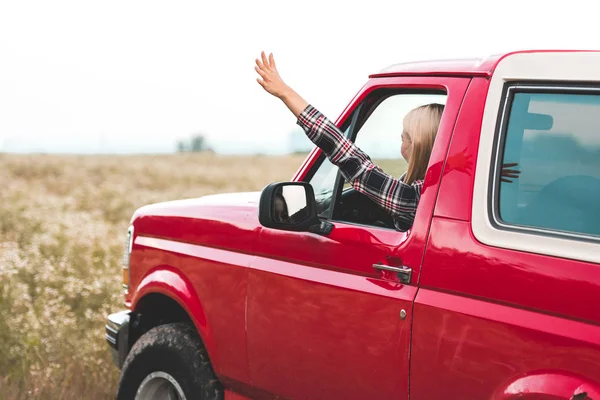 Schöne junge Frau fährt Auto auf Blumenfeld und winkt — Stockfoto