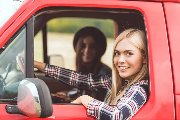 Seitenansicht von lächelnden jungen Freundinnen, die Auto fahren und in die Kamera schauen — Stockfoto