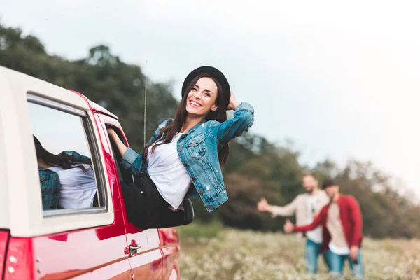 Young woman outstretching from car window while men hitchhiking blurred on background — Stock Photo