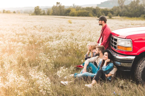 Seitenansicht einer Gruppe junger Autofahrer, die auf einem Blumenfeld sitzen und sich auf einen Oldtimer-LKW zurücklehnen — Stockfoto