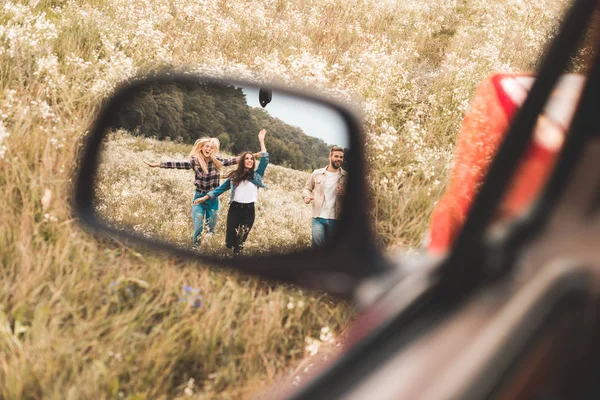 Mirror reflection of happy group of friends running by flower field — Stock Photo