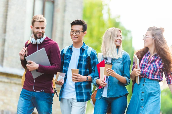 Portrait of smiling multiethnic students with backpacks walking in park — Stock Photo