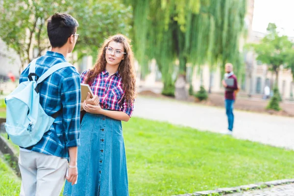 Vue partielle des étudiants multiraciaux ayant une conversation dans le parc — Photo de stock