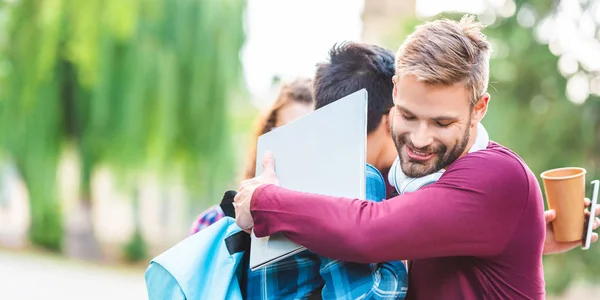 Vista parziale di studenti multiculturali con dispositivi digitali che si abbracciano nel parco — Foto stock