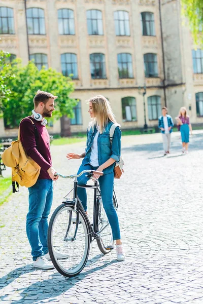 Estudantes com mochilas e bicicleta de pé na rua com universidade em segundo plano — Fotografia de Stock