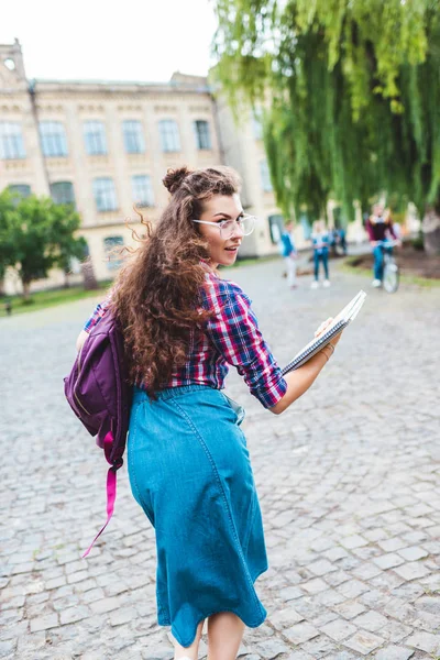 Visão traseira do jovem estudante em óculos com mochila e cadernos correndo na rua — Fotografia de Stock