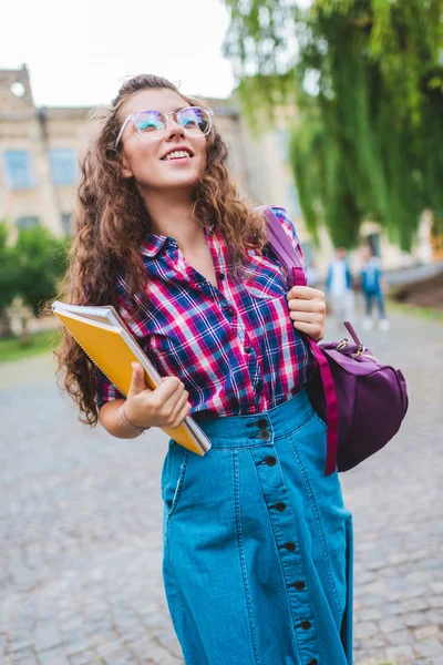 Portrait of smiling student in eyeglasses with notebooks running on street — Stock Photo