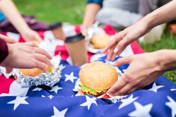 Visão parcial de amigos com hambúrgueres e bandeira americana na grama verde no parque — Fotografia de Stock