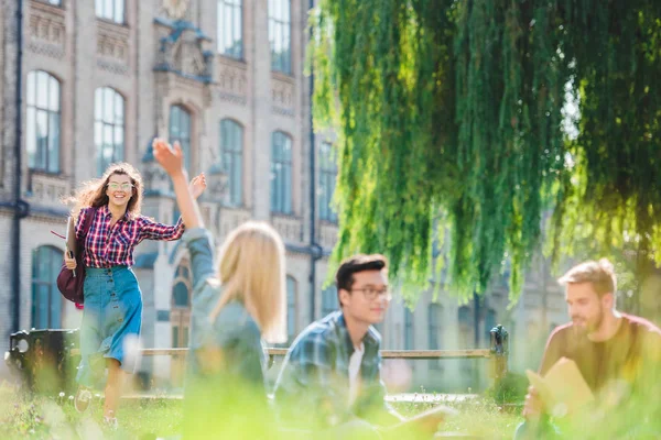 Мультирасовые студенты отдыхают в парке с университетом на заднем плане — стоковое фото