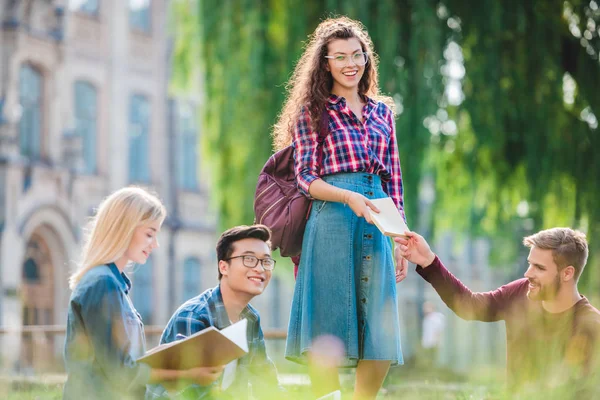 Estudantes multirraciais estudando no parque com universidade em segundo plano — Fotografia de Stock