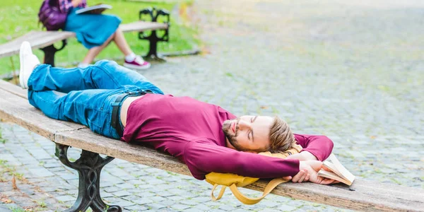 Вибірковий фокус студента, який спить на дерев'яній лавці в парку — стокове фото