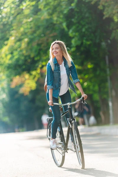 Smiling student with backpack riding bicycle on street — Stock Photo