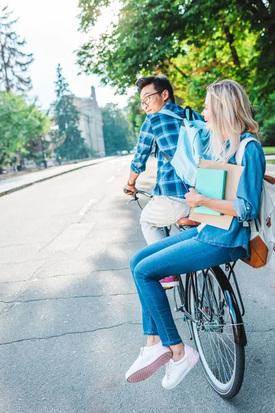 Estudiantes multirraciales sonrientes montar bicicleta juntos en la calle - foto de stock