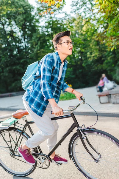 Side view of asian student with backpack riding bicycle on street — Stock Photo