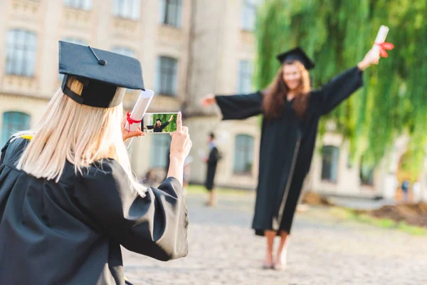 Частичный взгляд женщины, фотографирующей одноклассницу с дипломом во время окончания университета — стоковое фото
