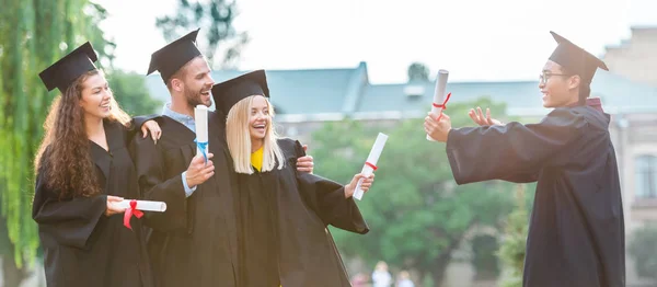 Retrato de graduados multirraciales felices con diplomas en la calle - foto de stock