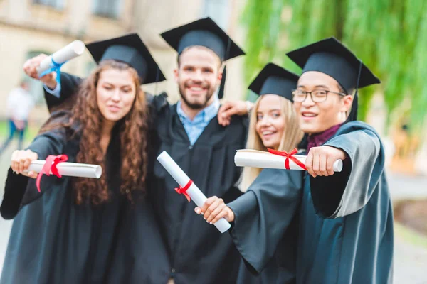 Retrato de graduados multirraciales felices con diplomas en la calle - foto de stock