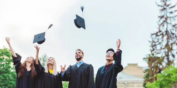 Portrait of happy multicultural graduates throwing caps up in park — Stock Photo