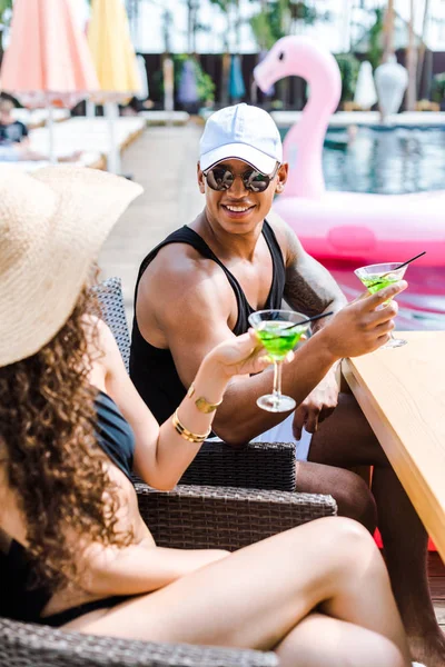 Boyfriend and girlfriend sitting with glasses of cocktails near swimming pool — Stock Photo