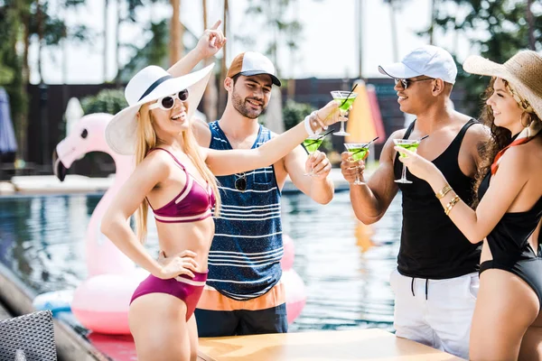 Amigos sonrientes tintineo con vasos de cócteles cerca de la piscina - foto de stock