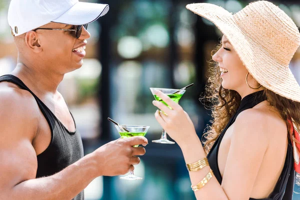 Side view of smiling boyfriend and girlfriend standing with cocktails near swimming pool — Stock Photo