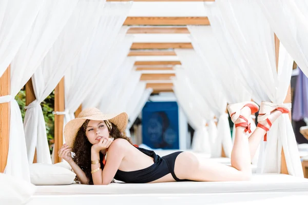 Chica atractiva en traje de baño negro tumbado en la tumbona y mirando hacia otro lado - foto de stock