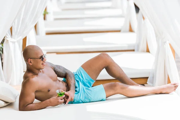 Shirtless tattooed muscular man lying on sun lounger with cocktail — Stock Photo