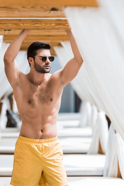 Handsome shirtless man in sunglasses standing near sun loungers — Stock Photo