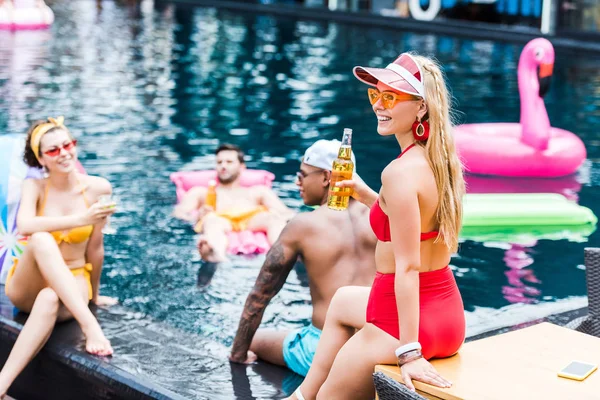 Jovem atraente com cerveja e seus amigos descansando na piscina — Fotografia de Stock