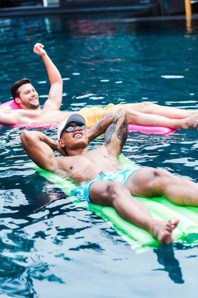 Dos amigos masculinos que descansan en colchones inflables en piscina - foto de stock