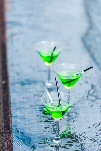 Vista de cerca de vasos con cócteles verdes con pajitas en la piscina - foto de stock