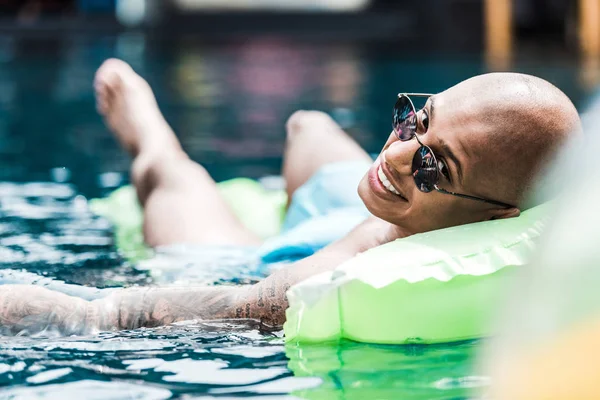 Hombre sonriente descansando en colchón inflable mirando la cámara en la piscina - foto de stock