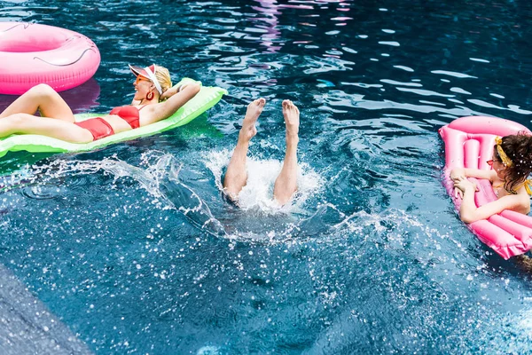Männerbeine ragen zwischen zwei Freundinnen auf aufblasbaren Matratzen im Schwimmbad aus dem Wasser — Stockfoto